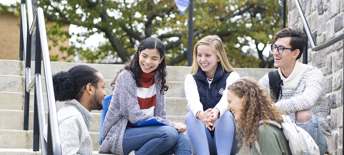 Group of 5 students sitting on stairs outside